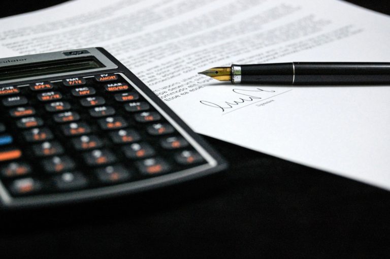 Une calculatrice posé sur une feuille de papier avec un stylo à côté, connotant le calcul du prêt immobilier.